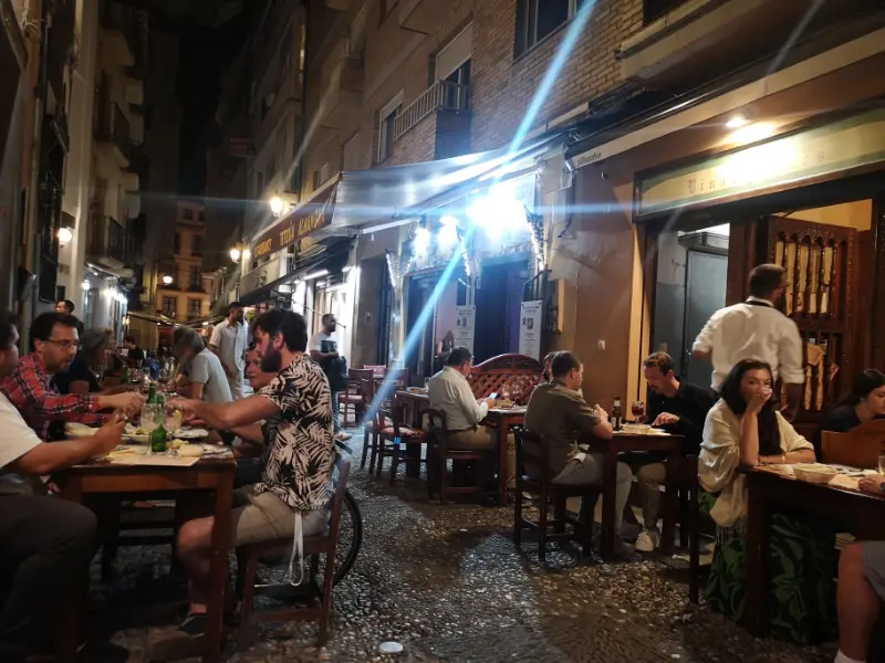 Mennesker spiser tapas på en tapasbar med borde på gaden i byen Granada i Spanien.